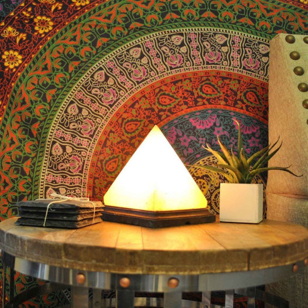 Pyramid Himalayan Pink Salt Lamp - Carved Crystal Glow illuminating a wooden table with colorful tapestry background.